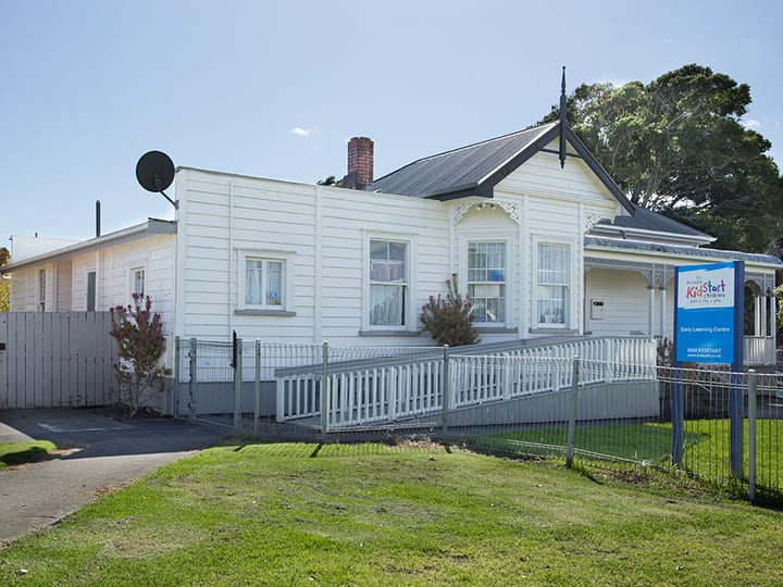 White timber villa exterior with pitched roof and decorative gable, white picket fence, green lawn