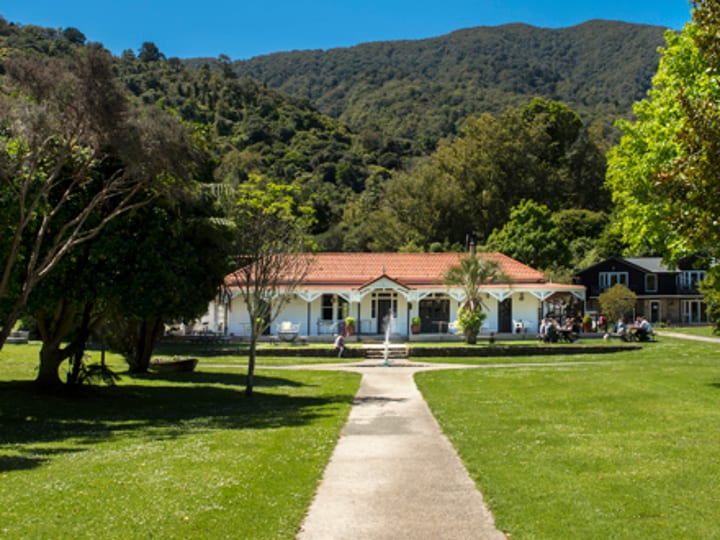 White homestead building on lawn with hills and trees behind