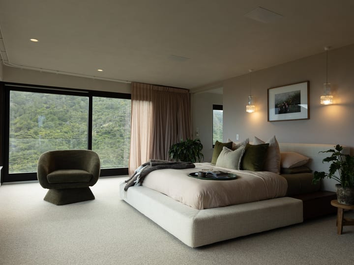 Large bedroom with low-profile bed, armchair and full-height windows to bush view