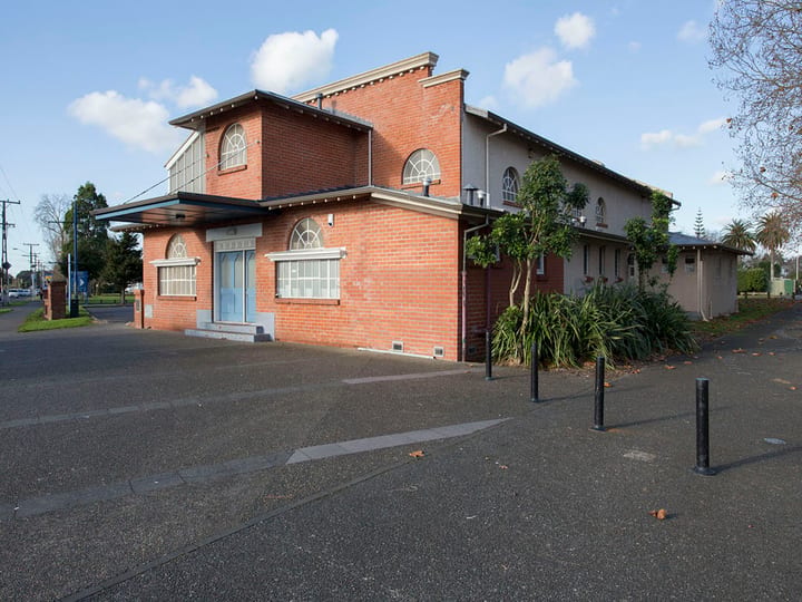 Red-brick two-storey community hall exterior with arched windows, car park and street frontage