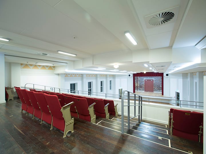 Tiered seating with red chairs facing a raised platform with red curtain