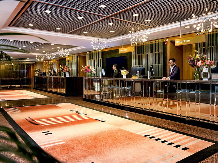 Hotel reception area with patterned stone floor, a long counter, and pendant chandeliers