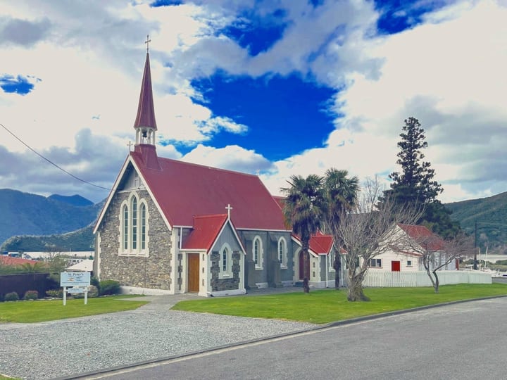 Stone church with red corrugated roof and steeple against blue sky