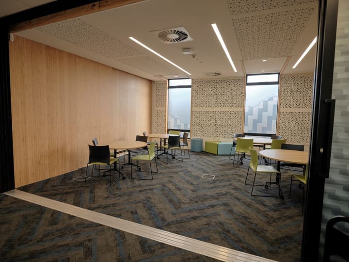 Modern meeting room with timber wall panels, round tables, green and black chairs, and patterned carpet