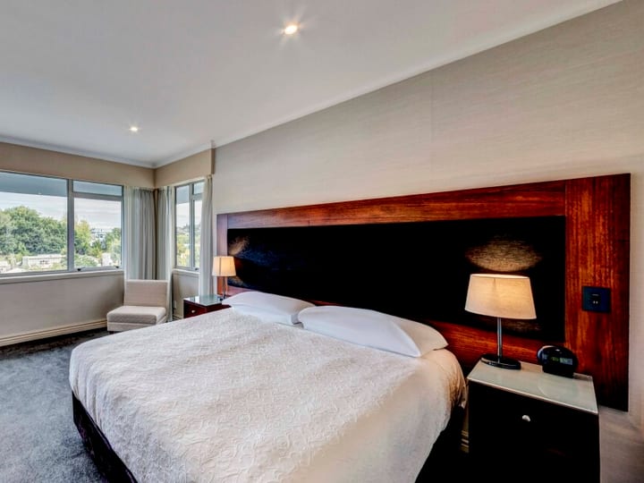 Hotel room with king bed, timber headboard, desk and city-view windows