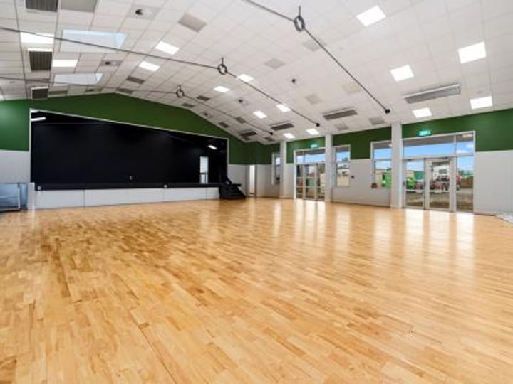 Full-length view of hall with raised stage, green accent walls and timber floor
