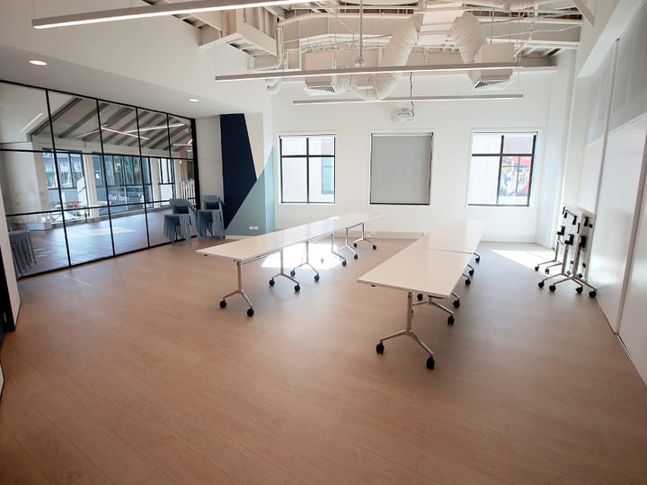 Meeting room with white folding tables, green chairs, and glass partition