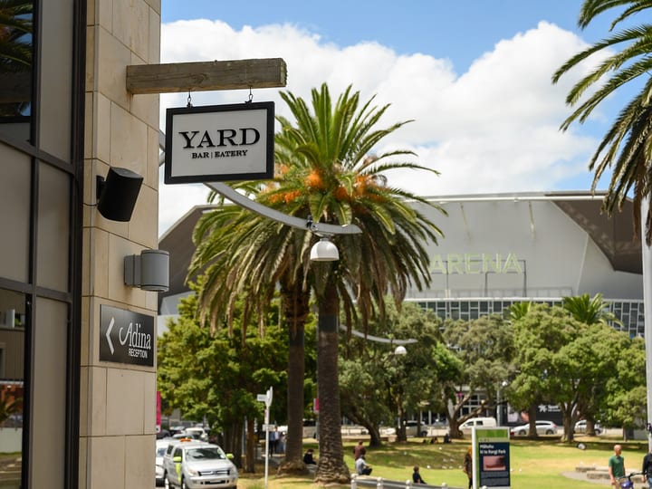 Stone-clad building exterior with hanging signage, trees and arena beyond
