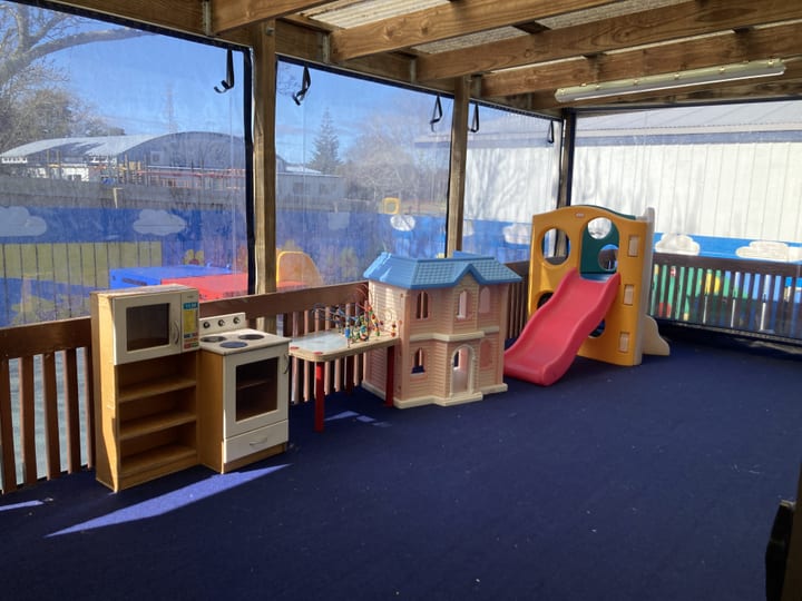 Covered outdoor play area with children's play equipment and blue flooring