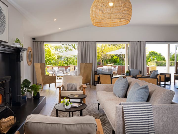 Light-filled lounge with fireplace, upholstered sofas, woven pendant, and open bifold doors to outdoor seating