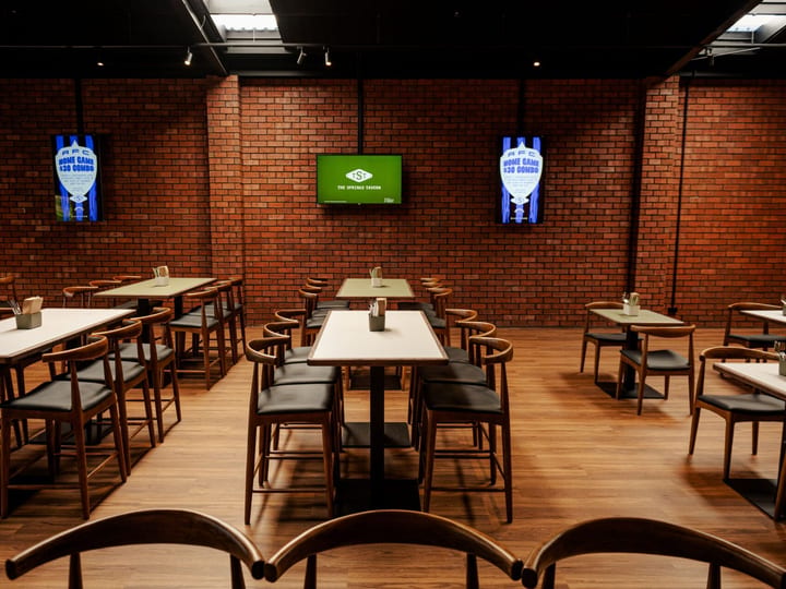 Exposed red brick room with white tables, bar-height seating and wall-mounted screens