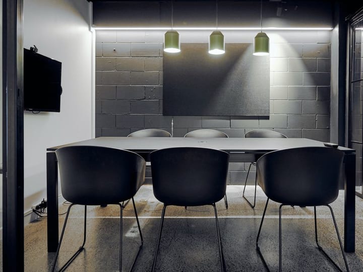 Dark meeting room with concrete block wall, black table, black chairs and green pendant lights