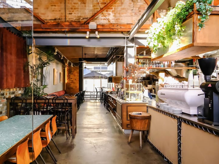 Industrial cafe interior with exposed brick, concrete floor, hanging plants, bar counter and seating