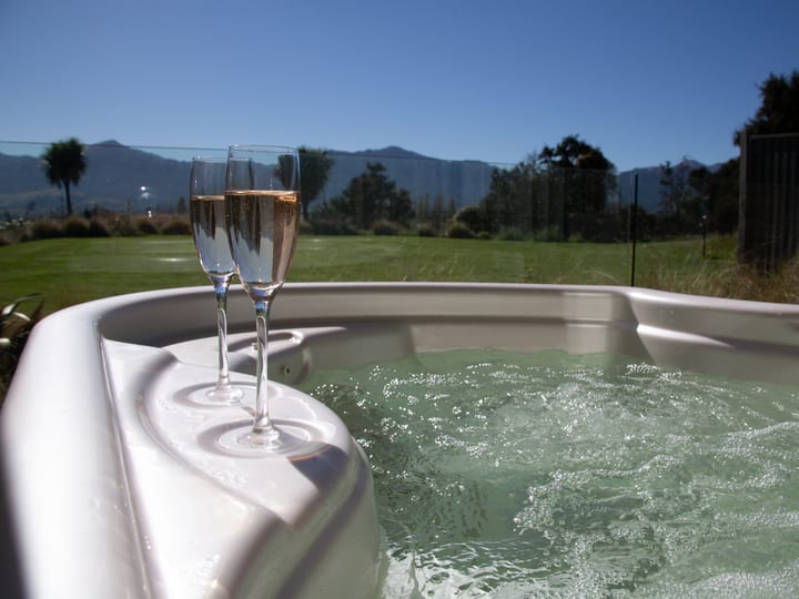 Outdoor spa pool with two champagne glasses on the edge and mountain views