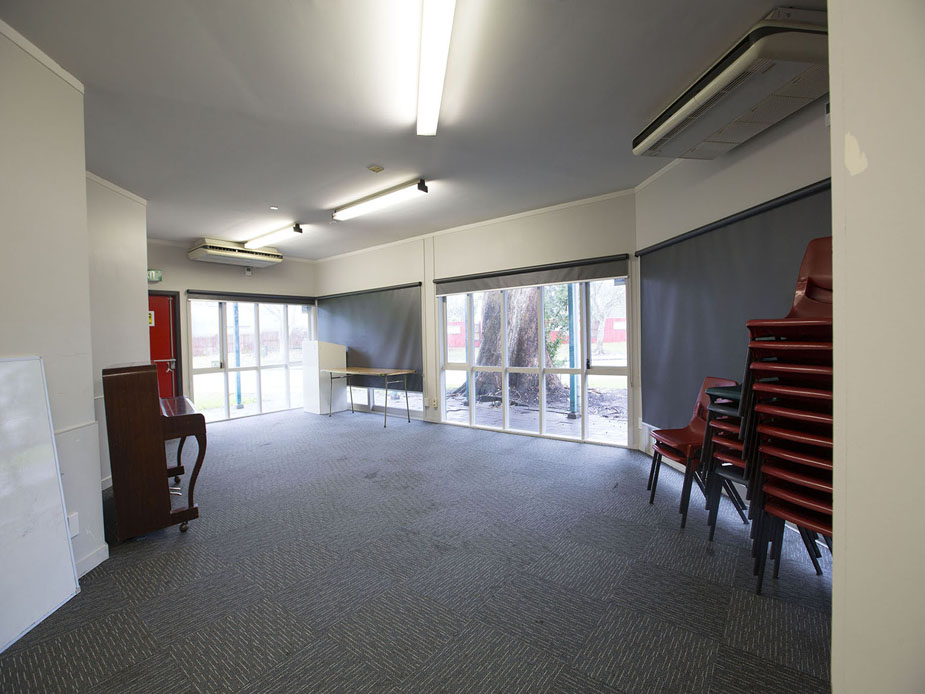 Carpeted room with stacked chairs, roller blinds, and upright piano
