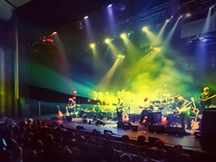Large theatre auditorium with stage lit in coloured lights and audience seating