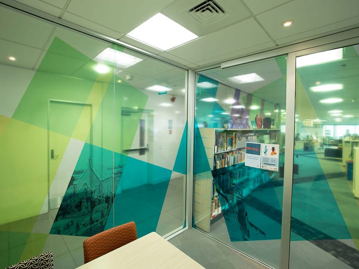 Glass-walled meeting room with colourful graphic panels and view to library floor