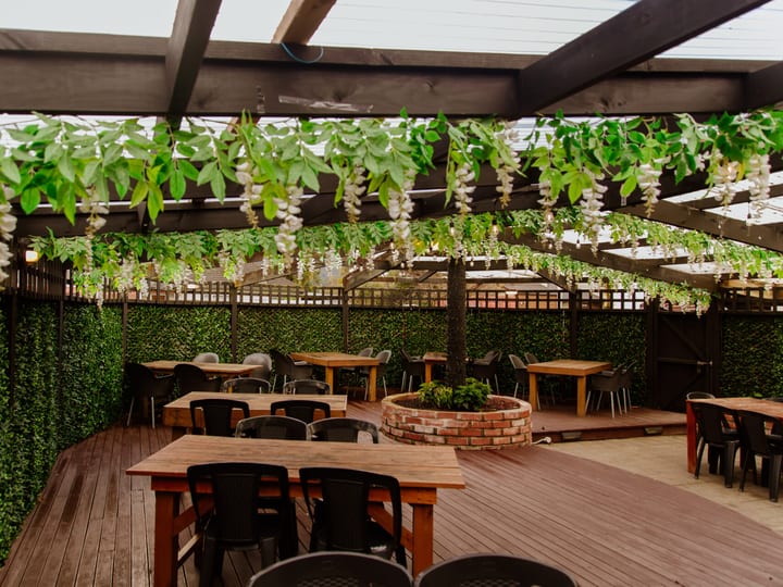 Timber deck with pergola, hanging foliage, and long dining tables