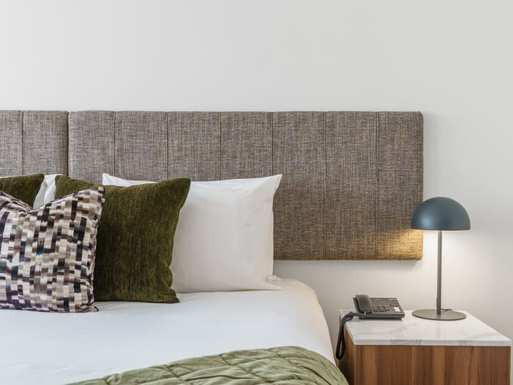 Hotel bedroom with upholstered headboard, textured green cushions and marble-top bedside table