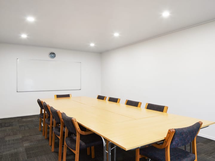 Plain meeting room with long timber table, upholstered chairs, whiteboard, recessed lighting