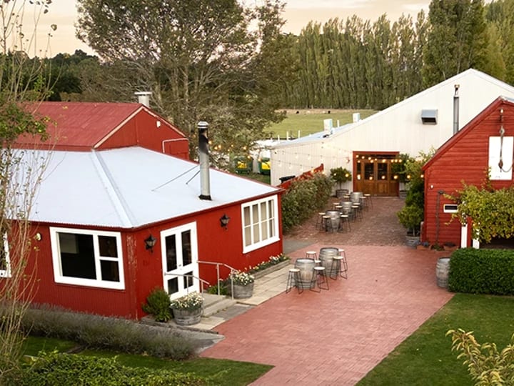 Elevated view of red timber buildings with courtyard seating and surrounding vineyard rows