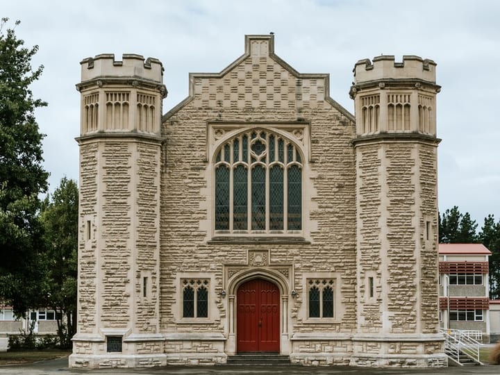 Stone Gothic building with corner turrets, arched windows, and red double doors