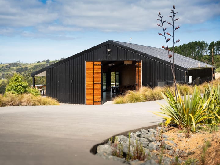 Black board-and-batten barn with timber doors and native planting on a hillside farm