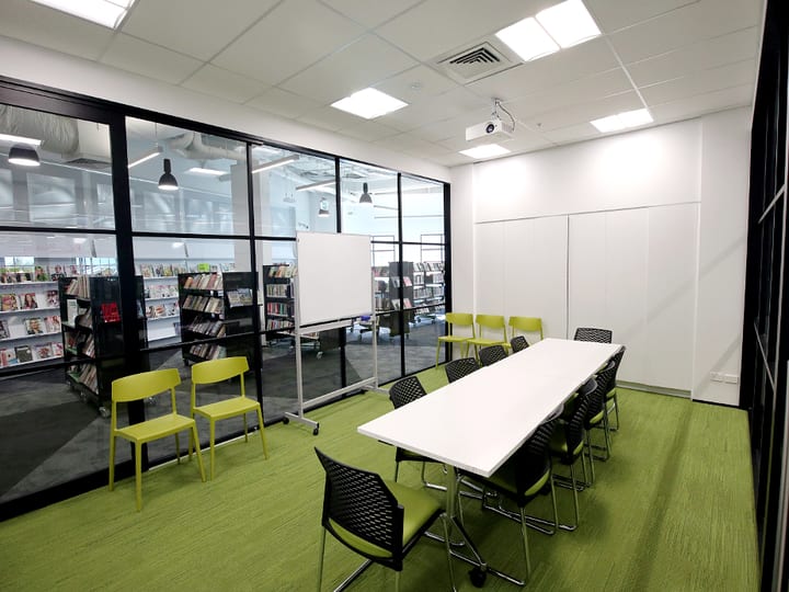 Meeting room with long white table, green chairs, and projector