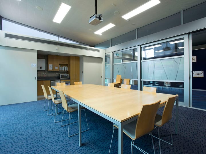 Meeting room with long table, chairs, projector, and kitchen area