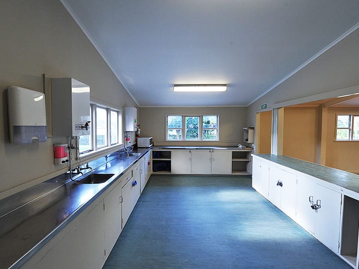 Long hall kitchen with stainless benchtops, white cabinetry and fluorescent lighting