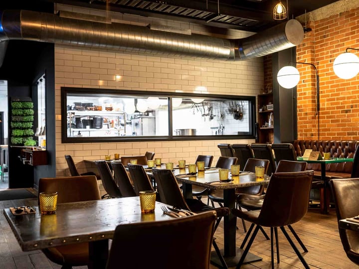 Brick-walled restaurant with dark timber tables, pendant lights, and pass window to kitchen