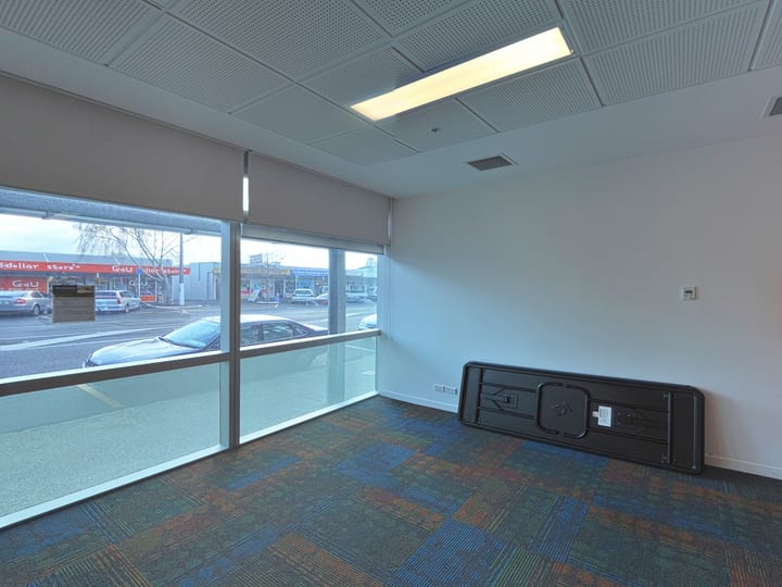 Empty carpeted room with full-height windows, roller blinds, and a folded table leaning against wall