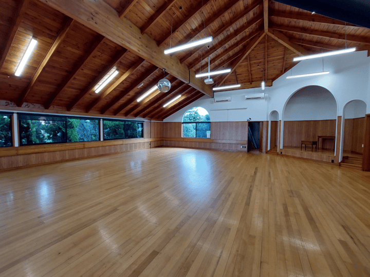 Empty hall with exposed timber roof trusses, polished floor and arched openings