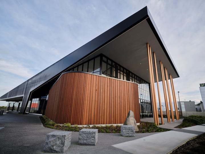 Contemporary building with curved dark timber cladding, metal roof canopy, and tall bronze columns