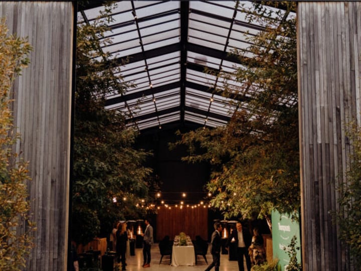 Glass-roofed pavilion interior with trees growing inside, viewed from entrance at night
