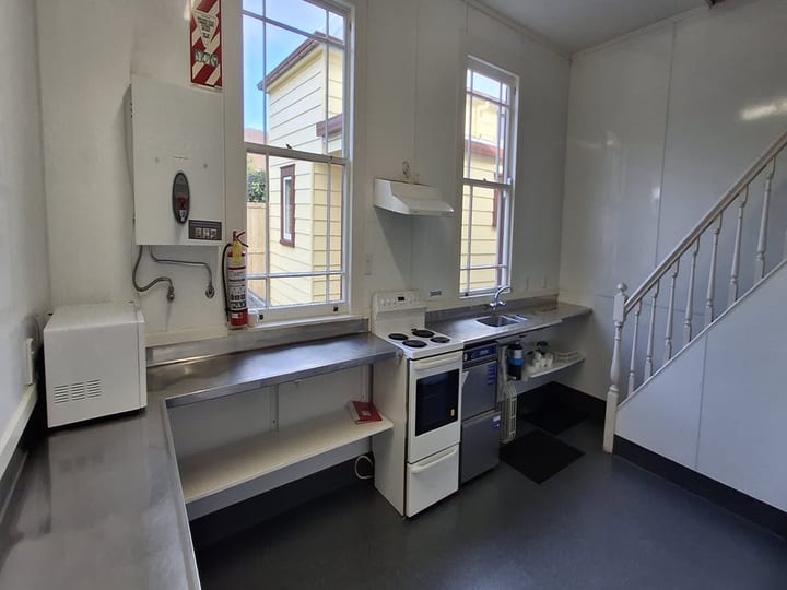 Basic kitchen with stainless benches, stove and dishwasher beside staircase