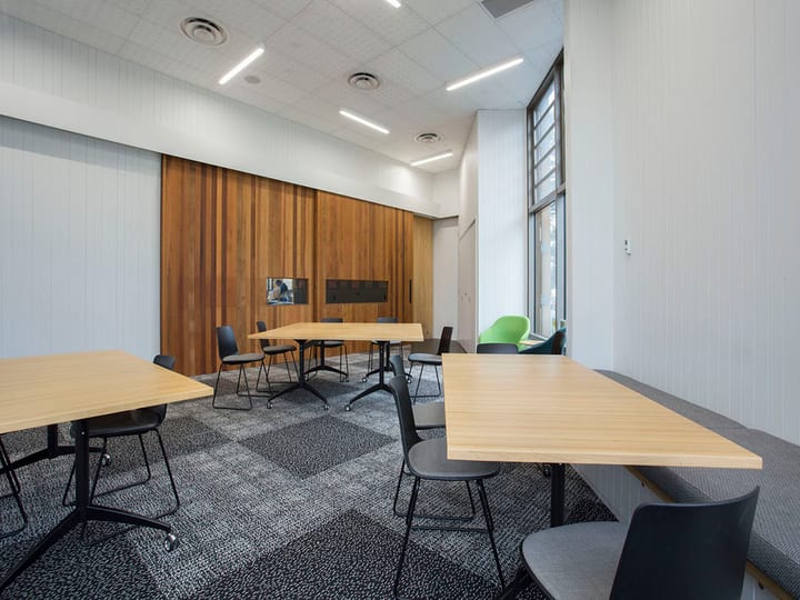 Meeting room with timber feature wall, light wood tables, dark chairs, screen, and bright window to garden