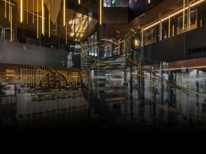 Dark double-height hotel lobby with gold lighting strips, bar area, and mezzanine level above