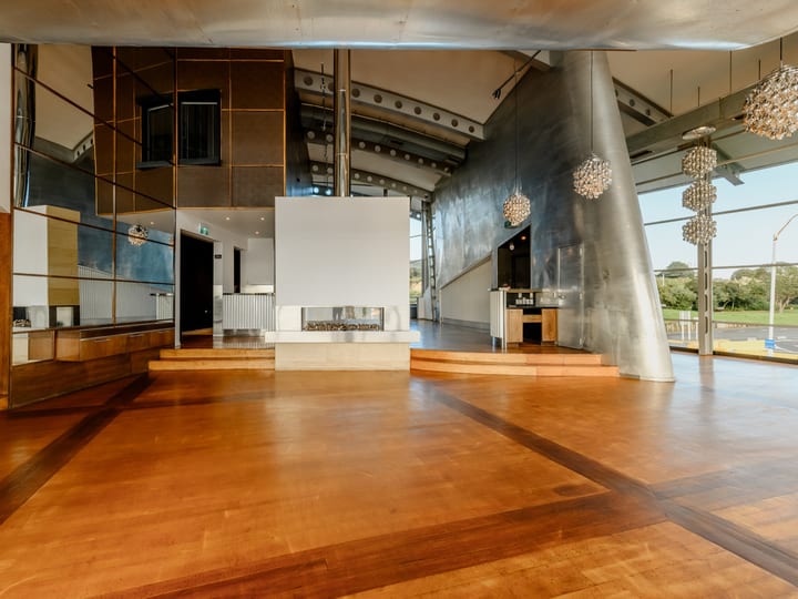 Open timber-floored hall with polished metal wall, central fireplace, and globe pendant lights