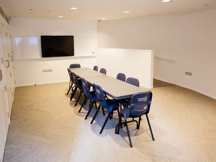Small meeting room with boardroom table, blue chairs and wall-mounted screen