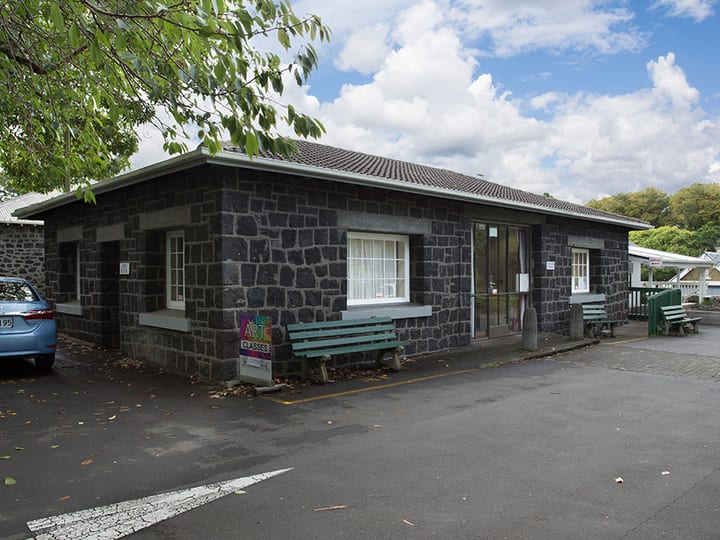 Small dark stone masonry building with bench seating at the entrance