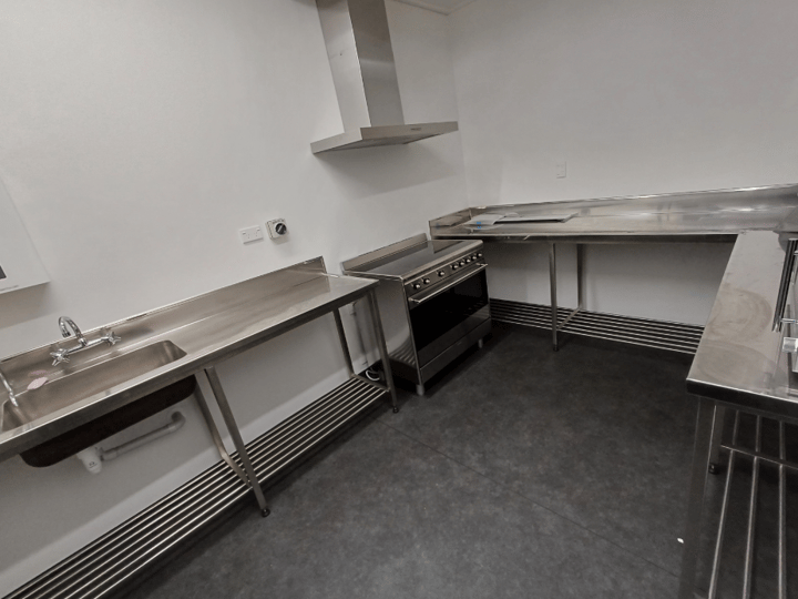 Compact stainless steel kitchen with oven range, extraction hood, and benches, dark floor