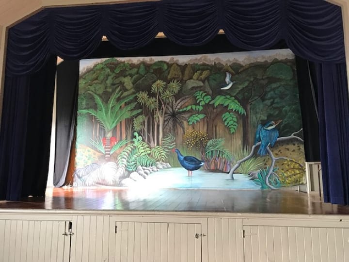 Raised platform with painted native-forest mural backdrop and dark curtains