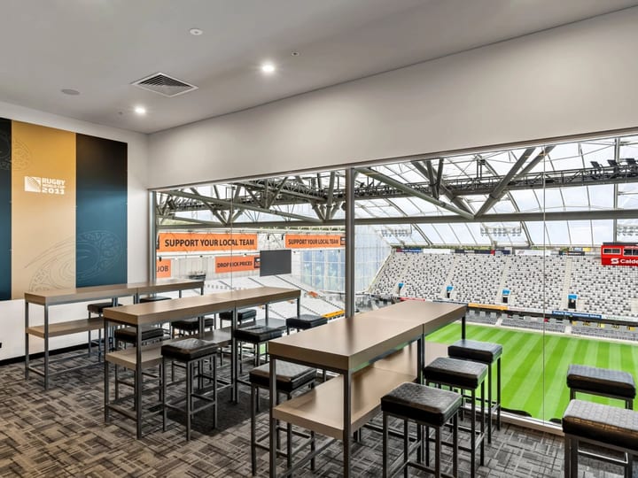 Stadium suite with high tables and bench seating, glass wall facing stadium interior