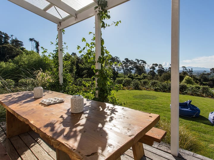 Timber deck with table under white pergola, lawns and garden leading to distant hills view