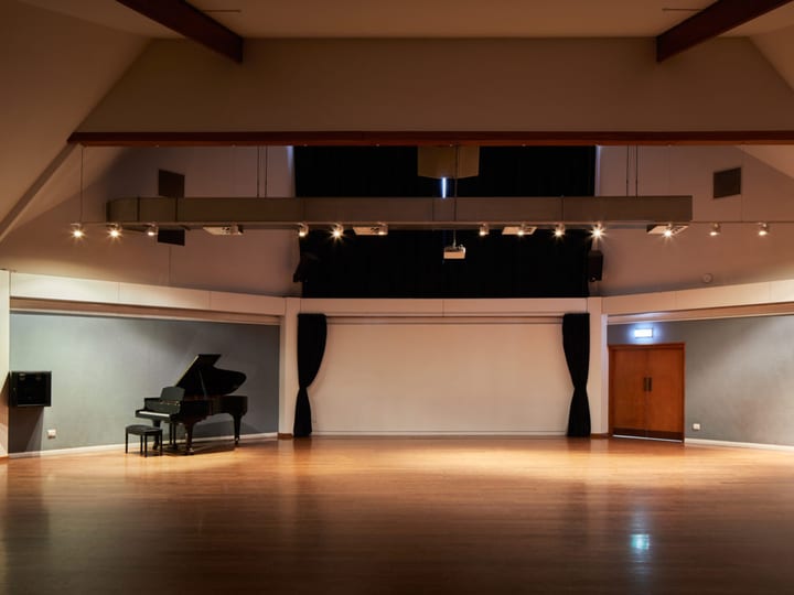 Large performance hall with timber floor, track lighting rig, grand piano and dark curtain backdrop