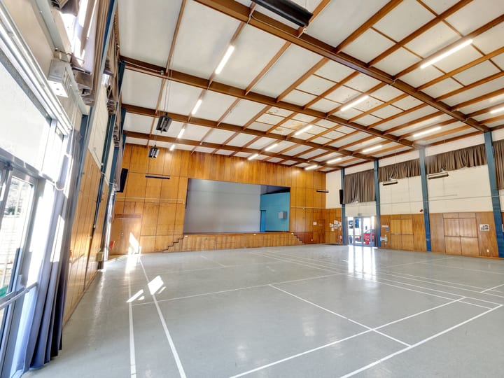 Large open hall with polished concrete floor, timber-panelled walls, high ceiling with steel trusses and projection screen