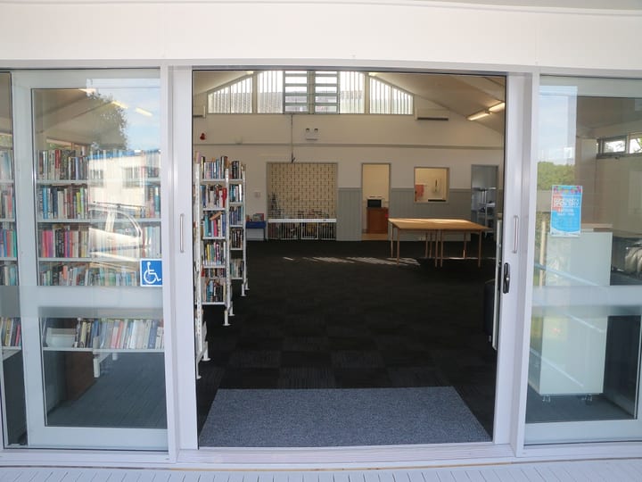 View through sliding glass doors into a hall interior with book shelving visible to the side