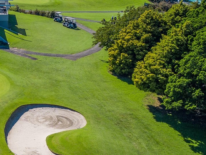 Aerial view of Akarana Golf Club clubhouse and course with sand bunkers and a topiary hedge spelling the club name