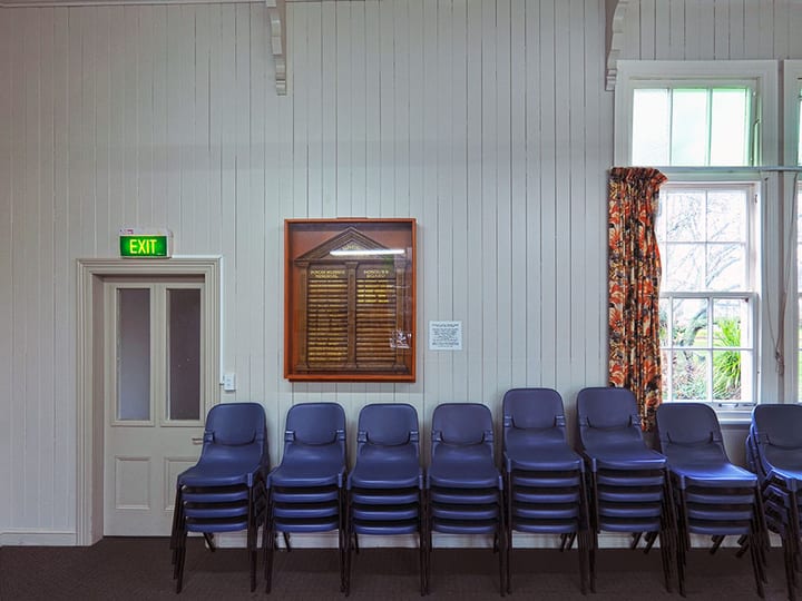 Hall interior with stacked chairs and honour board on white timber wall